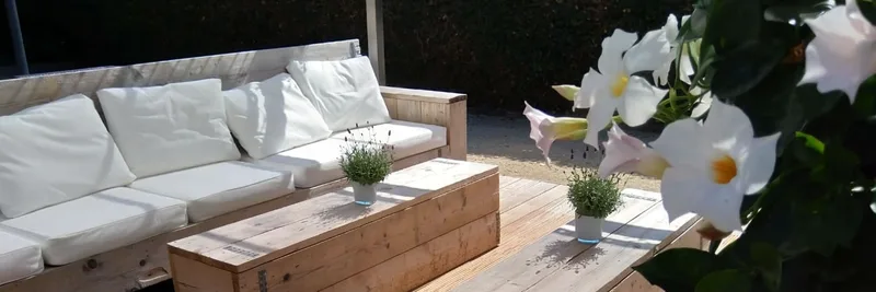 Houten lounge op het terras met witte kussens en bloemen
